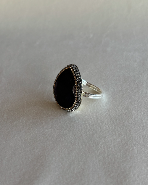 A silver ring featuring a large, teardrop-shaped Amethyst stone surrounded by a halo of small swarovski pavé stones, set on a gold base 
